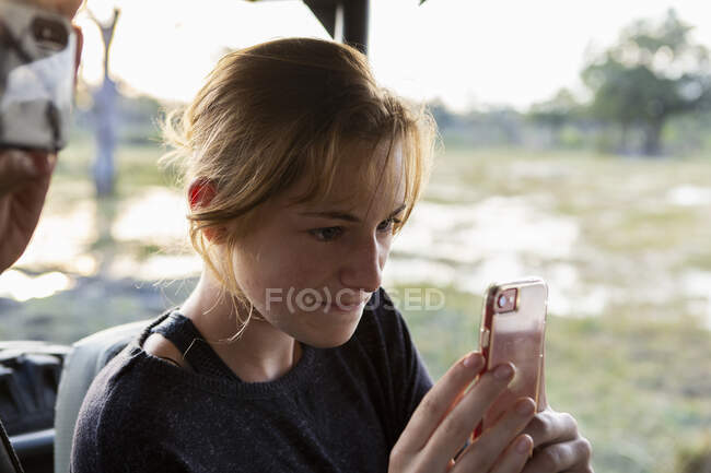 Teenage girl using smart phone to take a picture during a safari jeep drive. — Stock Photo