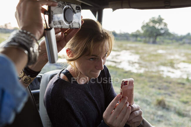 Adolescente usando un teléfono inteligente para tomar una foto durante un safari en jeep drive. - foto de stock
