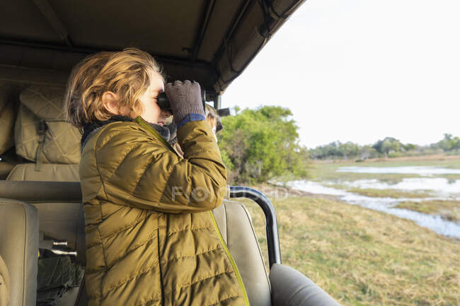 Young boy using binoculars standing in a safari jeep. — Stock Photo