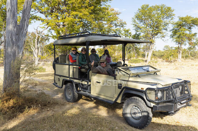 A safari jeep parked in the shade of a tree, people seated inside. — Stock Photo