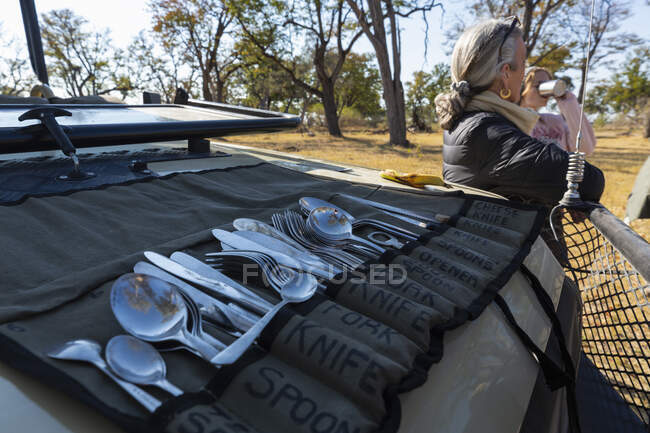 Uma parada de refeição no safári, pessoas tomando bebidas e um rolo de talheres espalhados no painel de um veículo de safári — Fotografia de Stock