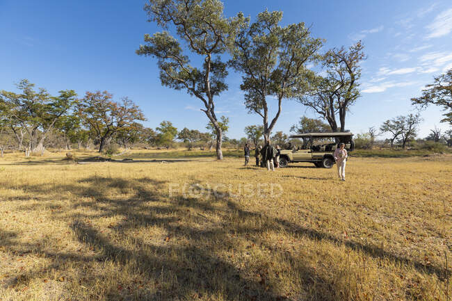 Ein Safari-Fahrzeug steht im Grasland, und die Menschen stehen drumherum. — Stockfoto