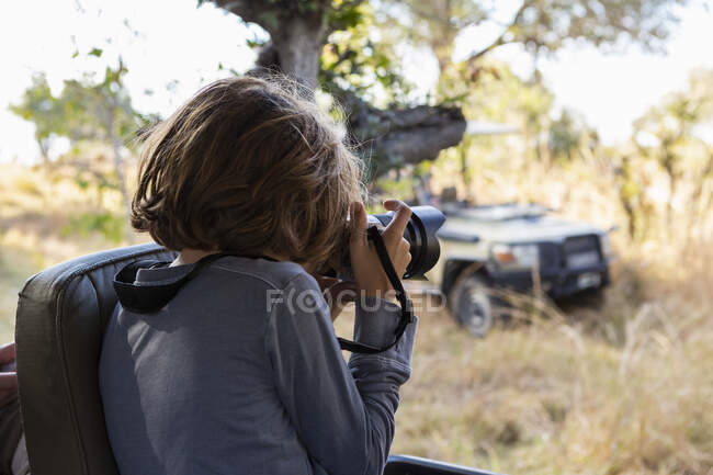 Giovane ragazzo utilizzando una grande macchina fotografica durante una jeep drive su safari — Foto stock