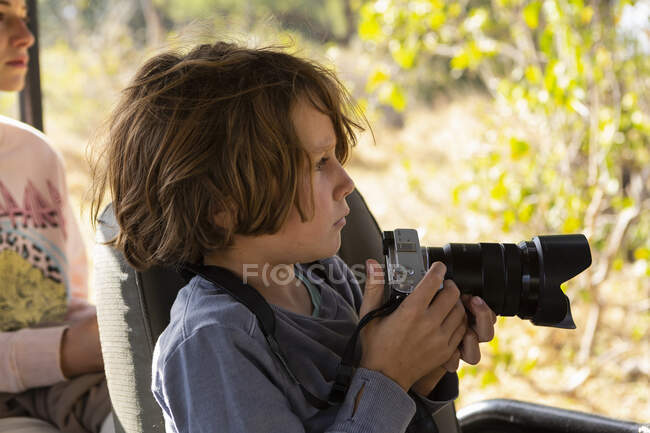 Niño usando una cámara sentada en un jeep - foto de stock