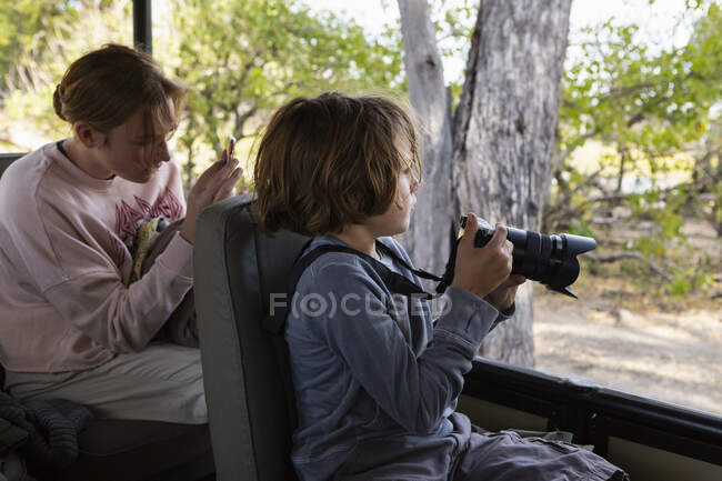 Giovane ragazzo utilizzando una fotocamera seduta in una jeep — Foto stock