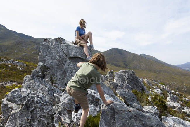 Una adolescente y su hermano escalando formaciones rocosas en el paisaje de las montañas Klein - foto de stock