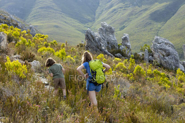 Teenage girl and a boy walking along a path through vegetation and rocks in the fynbos — Stock Photo