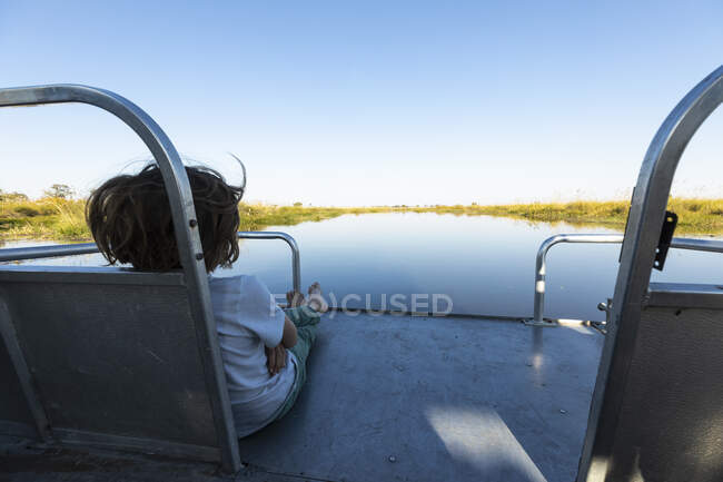 Um menino em uma lancha viajando ao longo de uma via navegável no delta do Okavango — Fotografia de Stock