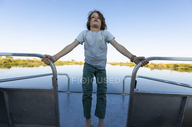 Ein Junge auf einem Motorboot, das auf einer Wasserstraße unterwegs ist und sich an einem Geländer festhält. — Stockfoto