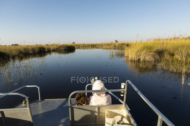 Two children seated on a boat, looking out over calm waters and flat landscape — Stock Photo