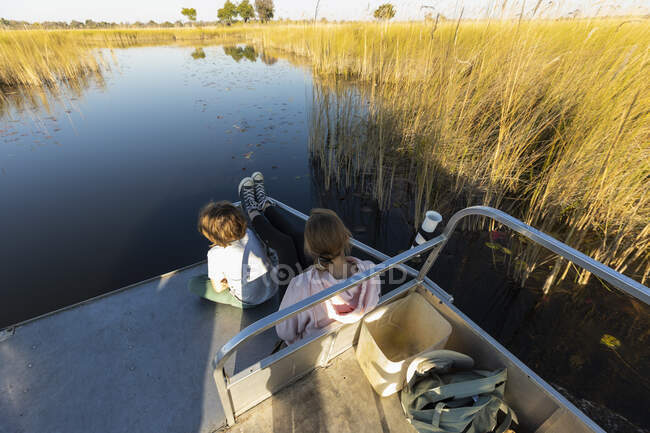Двоє дітей сидять на кормі човна, що тече по тихому водному шляху . — стокове фото