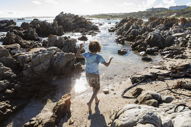 Niño de ocho años explorando una playa rocosa - foto de stock