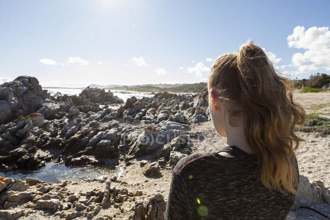 Adolescente olhando para fora sobre uma praia e pedras irregulares para o oceano — Fotografia de Stock