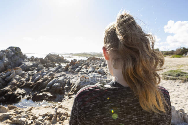Adolescente olhando para fora sobre uma praia e pedras irregulares para o oceano — Fotografia de Stock