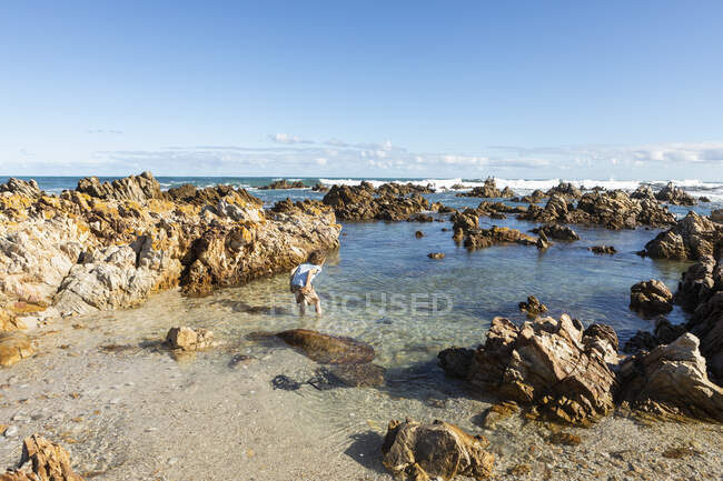Young boy exploring a beach and rockpools on a jagged rocky coastline. — Stock Photo