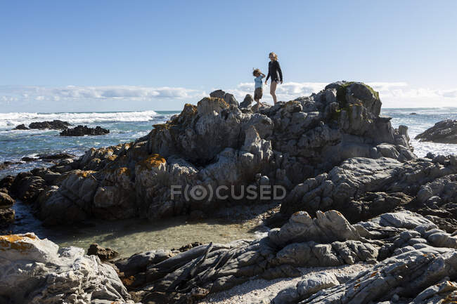 Двое детей, девочка-подросток и восьмилетний мальчик исследуют зазубренные камни и каменистые бассейны на пляже. — стоковое фото