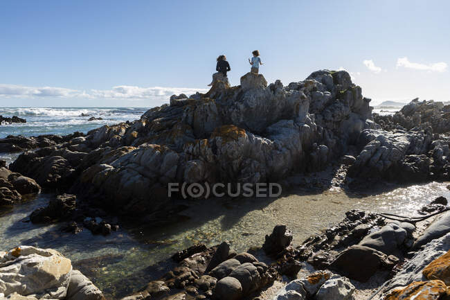 Deux enfants, une adolescente et un garçon de huit ans explorant les rochers et les rochers déchiquetés sur une plage. — Photo de stock