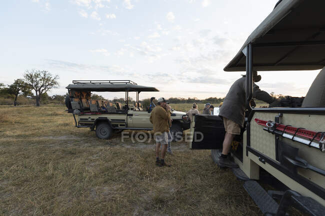 Gruppe von Menschen, die um Safari-Fahrzeuge auf einer frühmorgendlichen Pirschfahrt stehen — Stockfoto