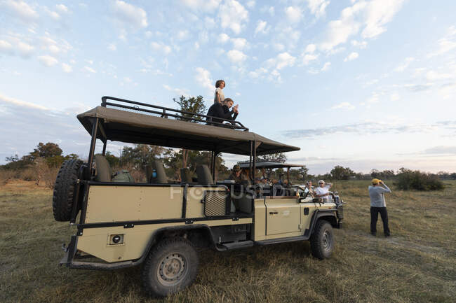 Groupe de personnes autour des véhicules de safari sur une promenade de jeu de lever de soleil — Photo de stock