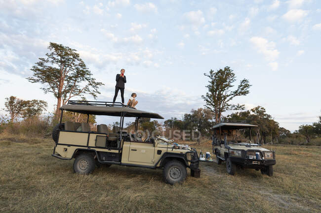 Dos niños en el techo de un vehículo de safari en una unidad de juego del amanecer - foto de stock