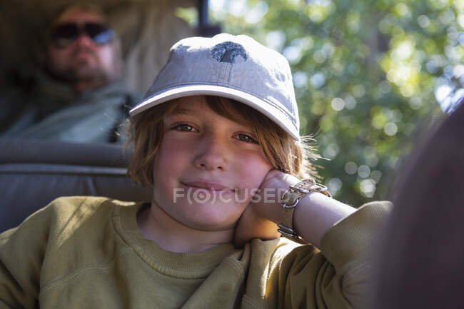 Un chico sentado en un jeep apoyado en su codo en un jeep de safari. - foto de stock