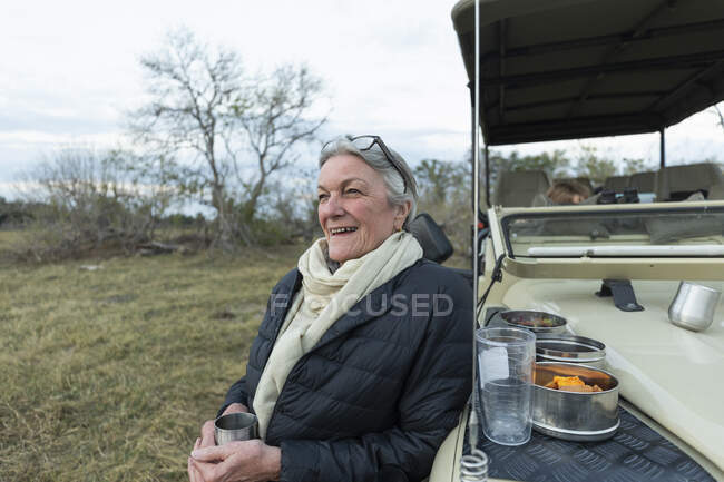 Senior woman smiling, standing by a jeep at early morning, — Stock Photo