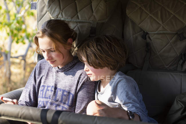 Adolescente e um menino sentado em um jipe olhando para um telefone inteligente. — Fotografia de Stock