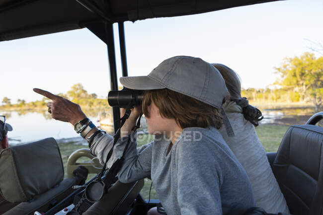Niño en un jeep safari mirando a través de los prismáticos. - foto de stock