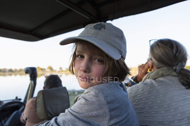 Niño en un jeep safari con gorra de béisbol mirando a la cámara - foto de stock