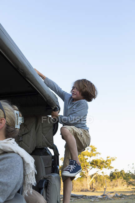 Un niño trepando por el lado del vehículo safari - foto de stock