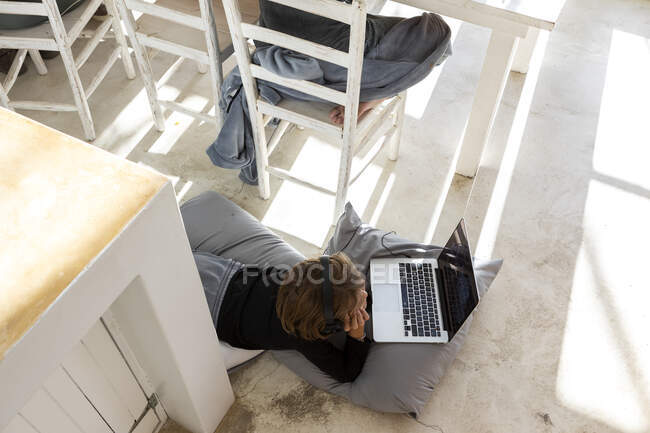 Eight year old boy lying on cushions, chin on hands, watching a laptop screen, doing homework. — Stock Photo