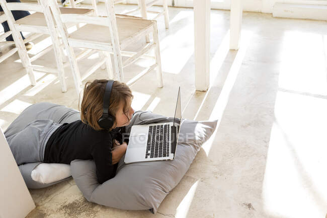Eight year old boy lying on the floor on cushions using a laptop — Stock Photo