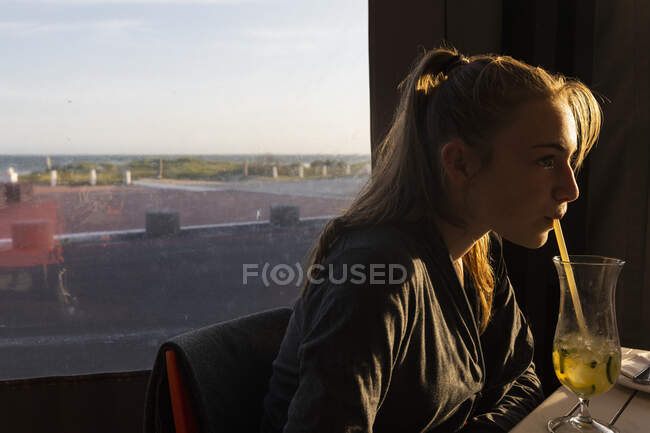 Дівчина-підліток сидить у пляжному кафе, випиваючи соломинку — стокове фото