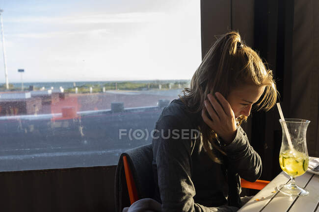 Девочка-подросток сидит в пляжном кафе, потягивая напиток через соломинку — стоковое фото