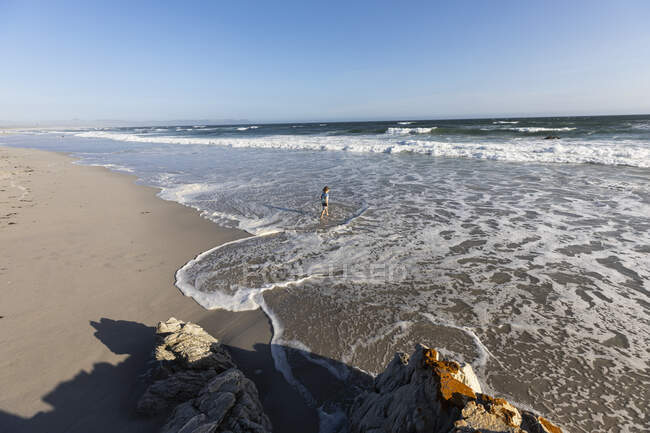Menino brincando no surf na beira da água em uma praia de areia larga — Fotografia de Stock