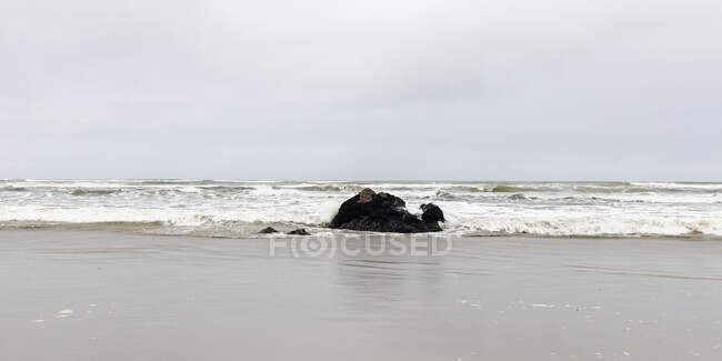 Affioramento roccioso nel surf in una spiaggia di sabbia. — Foto stock