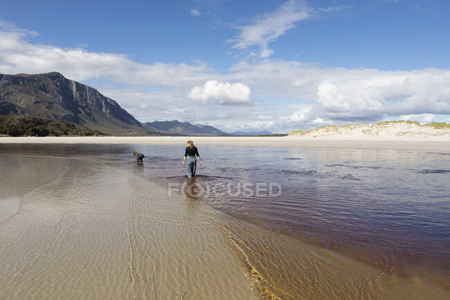 Teenager Mädchen und kleiner Junge an einem offenen Sandstrand, der durch flaches Wasser watet. — Stockfoto