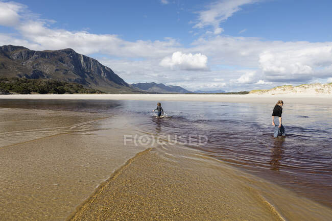 Adolescente menina e menino em uma praia de areia aberta percorrendo águas rasas. — Fotografia de Stock