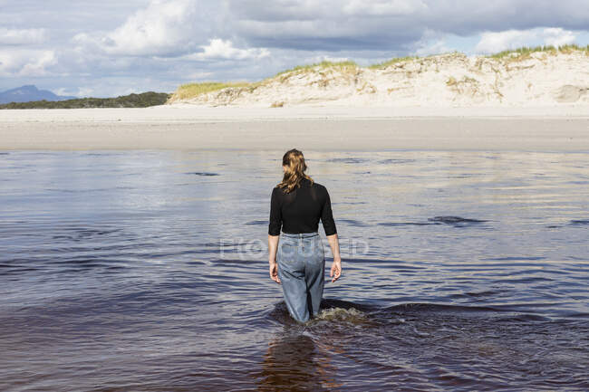 Une adolescente pataugeant dans un canal d'eau sur une large plage de sable fin. — Photo de stock