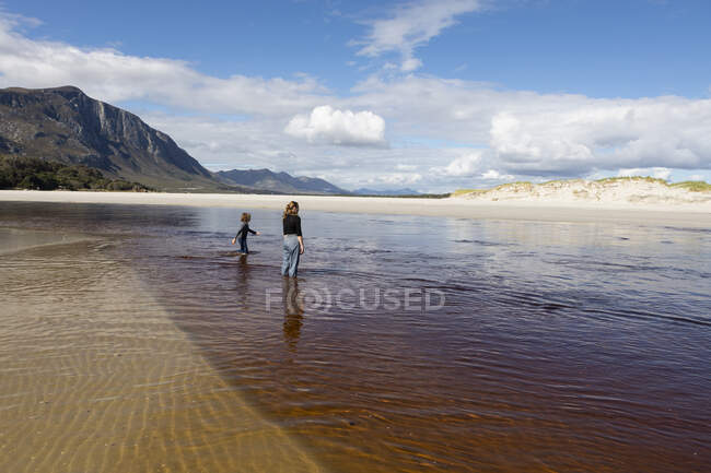 Девочка-подросток и мальчик на открытом песчаном пляже, плывущие по мелководью. — стоковое фото