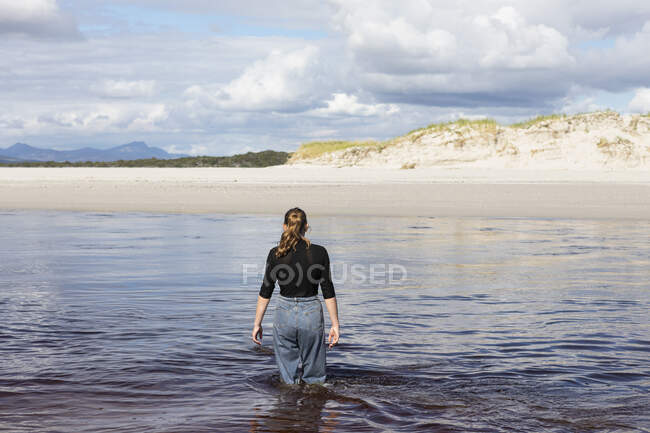 Ein Teenager-Mädchen watet durch einen Wasserkanal an einem breiten Sandstrand. — Stockfoto
