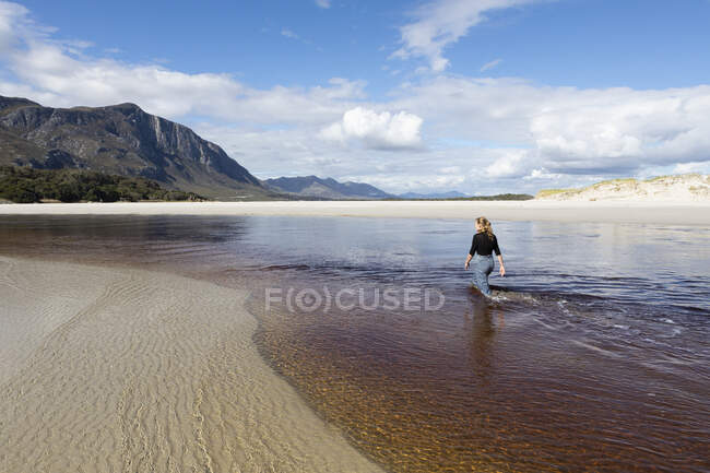 Uma adolescente percorrendo um canal de água em uma ampla praia de areia. — Fotografia de Stock