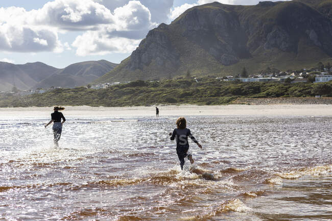 Teenagermädchen und ein Junge rennen durch seichtes Wasser an einem breiten Sandstrand — Stockfoto