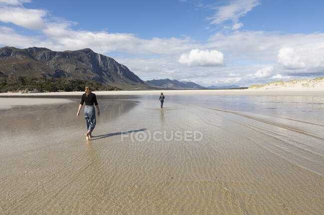Adolescente y su hermano menor caminando a través de una amplia playa - foto de stock