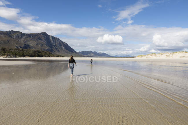 Дівчинка-підліток і молодший брат, що йде через мілководдя на піщаному пляжі — стокове фото
