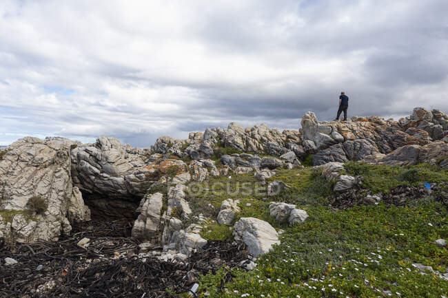 Man wandering along a jagged coastline under a overcast sky. — Stock Photo