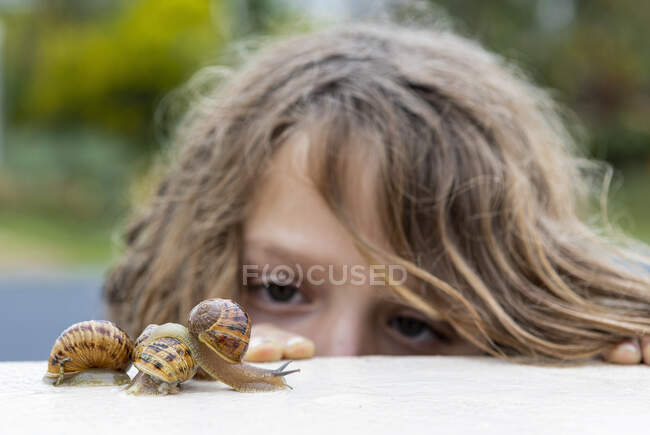 Jeune garçon regardant de près les escargots sur un mur. — Photo de stock