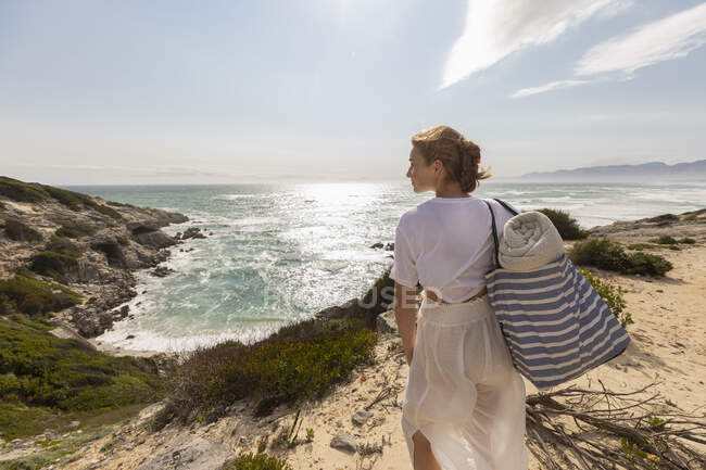 Teenage girl standing on top of a cliff looking over the coastline and inlet. — Stockfoto