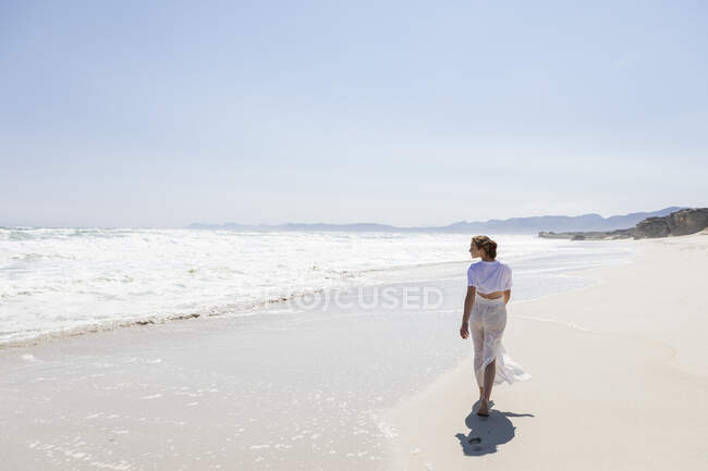 Teenage girl walking on a sandy beach at the water's edge — Foto stock