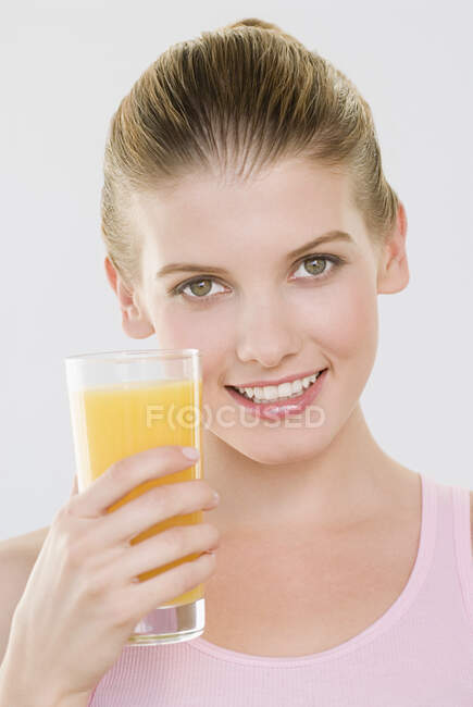 Mulher olhando para câmera segurando vidro de suco de laranja. — Fotografia de Stock